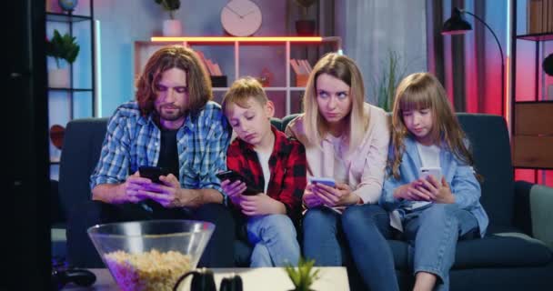 Likable unhappy friendly family sitting on the couch at home and applying their own phones as there is nothing to watch on TV set — Stock Video