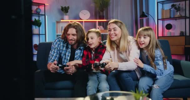 Atraente feliz sorrindo família emocional celebrando a vitória em videogames com as mãos levantadas enquanto passa o lazer conjunto em casa à noite — Vídeo de Stock