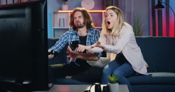 Mänsklig reaktion på seger där stilig rolig skäggig kille firar vinna i videospel över sin blonda flickvän som gör förvirrad ansikte och tror inte på förlust — Stockvideo