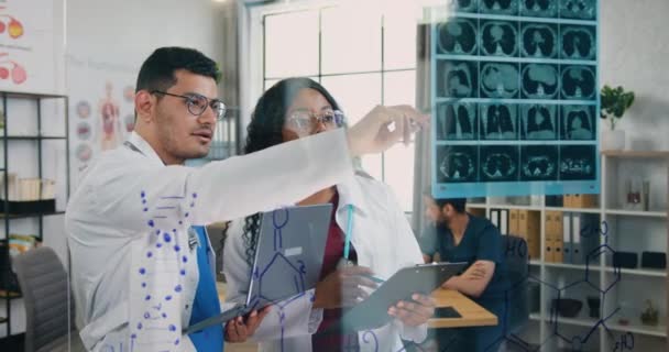 Medizin-Konzept, wo attraktive professionelle erfolgreiche gemischte Rasse männliche und weibliche medizinische Mitarbeiter mit Röntgenuntersuchungen in der Arztpraxis auf dem Hintergrund ihrer Kollegen, die an der — Stockvideo