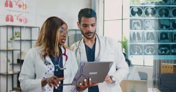 Attractive professional skillful adult multiracial doctors working with results of x-ray scan and information about patients diagnosis on laptop screen in medical office — Stock Video