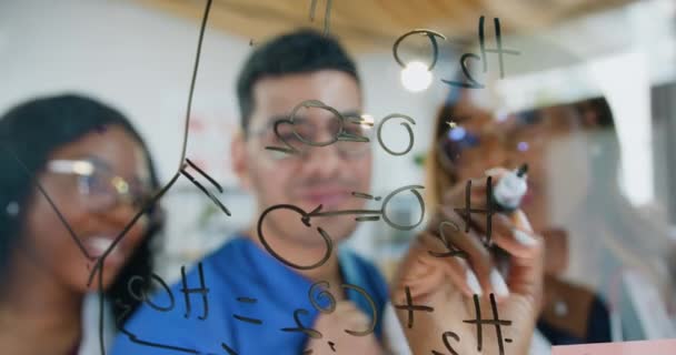 Умілі серйозні хіміки або вчені, які працюють над новою формулою і пишуть її на скляній дошці в науковій лабораторії, повільний рух — стокове відео