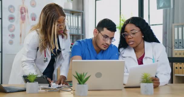 Close up of likable skilled professional diverse medical team which working together in clinic room with datas from medical card and results of computer diagnosis — Stock Video