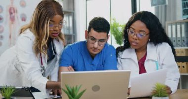 Tıbbi işbirliği konsepti, deneyimli karışık ırk erkek ve kadın doktorlarının hasta teşhisi hakkında beyin fırtınası yapmaları ve dizüstü bilgisayar kullanmaları.