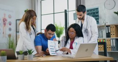 Tıbbi ekip çalışması konsepti. Deneyimli, zeki, çeşitli doktorların tıp odasında bilgisayar aracılığıyla video toplantısı düzenlemesi ve DNA bilgilerinin sonuçlarını açıklaması.