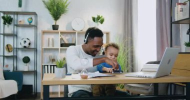 Çekici, mutlu, siyah derili, kulaklıklı babanın iş yerinde küçük oğluyla oturup siyah arabasıyla oynadığı ebeveynlik konsepti.