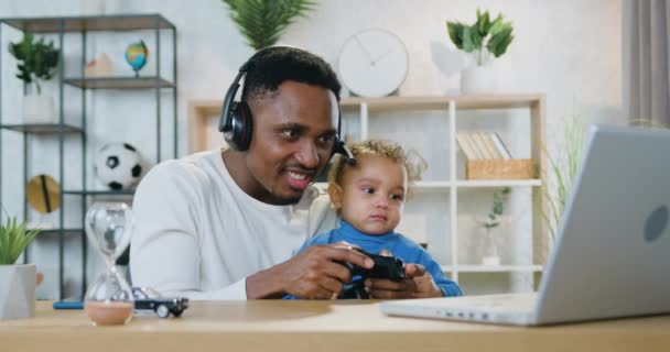 Parenthood concept where handsome smiling happy emotional caring black-skinned dad playing videogames on laptop together with small son and celebrating victory — Stock Video