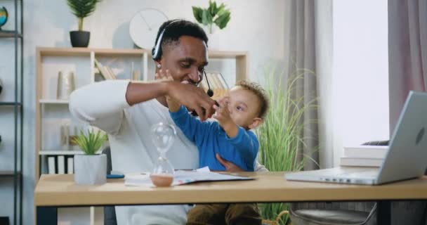 Concept de garde d'enfants où attrayant heureux souriant jeune père à la peau noire jouer avec son petit fils en utilisant une voiture jouet, assis à la table dans une chambre confortable — Video