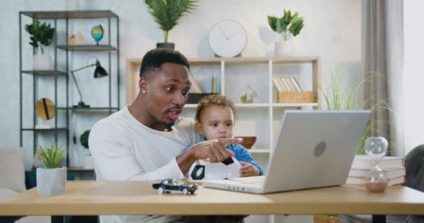 Bello felice emotivo cura papà dalla pelle nera tenendo il suo piccolo figlio carino sulle ginocchia quando si guarda la partita di calcio sul computer portatile e celebrando gol segnato, cura dei bambini e concetto di paternità — Video Stock