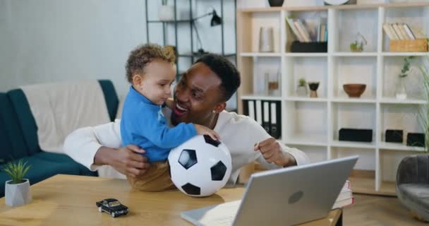 Aantrekkelijk vrolijk gelukkig zorgzame jonge Afrikaanse vader-voetbal fan verheugen van de overwinning van favoriete team en knuffelen zijn schattige kleine zoon, kinderopvang en vrijetijdsconcept — Stockvideo