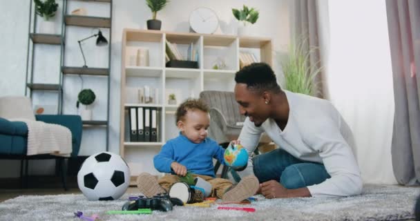 Fešák usměvavý šťastný starostlivý mladý africký americký táta baví spolu se svým roztomilým chlapeček doma, pohled zepředu — Stock video