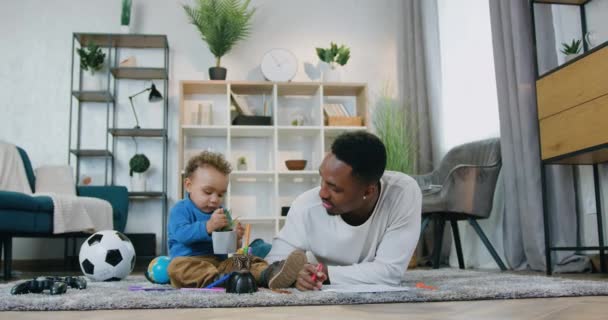 Concepto de cuidado infantil donde el buen aspecto feliz amante de 30 años de piel negra papá pasar su tiempo junto con lindo hijo pequeño en casa — Vídeo de stock