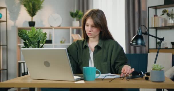 Attractive confident skilled 25-aged female worker sitting at her workplace at home office and working with financial report and datas on computer — Stock Video