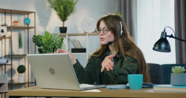 Симпатичная и уверенная в себе молодая женщина-фрилансер сидит перед компьютером дома и проводит онлайн-встречу со своей аудиторией — стоковое видео