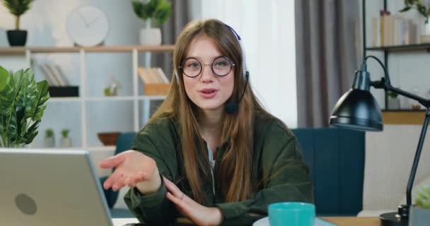 Conceito de fluxo de trabalho de boa aparência sorridente menina feliz em fone de ouvido sem fio segurando conferência on-line de home office e falando em câmera para o seu público — Vídeo de Stock