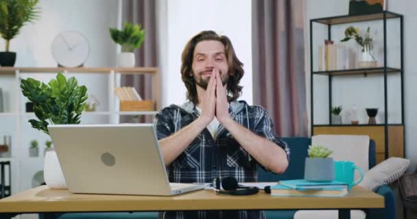 Attraktives Lächeln, friedlicher junger bärtiger Mann, der sich entspannt und Gyan Mudra Symbole herstellt, wenn er an seinem Arbeitsplatz meditiert, während er zu Hause am Computer arbeitet — Stockvideo