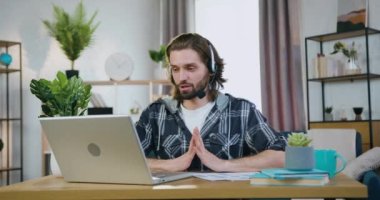 Uzaktan çalışma konsepti. Yakışıklı, kendine güvenen, sakallı, kulaklıklı profesyonel ofis çalışanı. İç işlerinden iş arkadaşlarıyla video görüşmesi yapıyor.