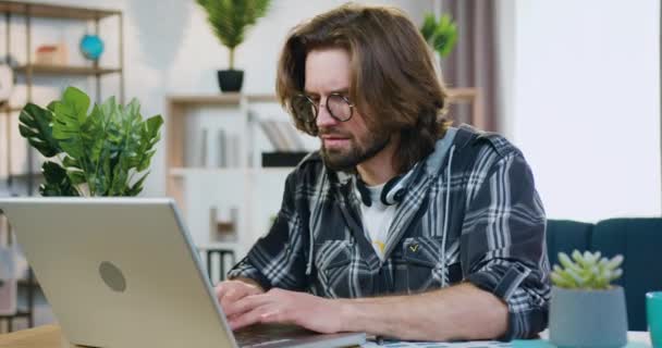 Όμορφος βέβαιος σοβαρή επιτυχημένη νεαρός γενειοφόρος ελεύθερος επαγγελματίας κάθεται μπροστά από τον υπολογιστή στο σπίτι και πληκτρολογώντας κείμενο στο πληκτρολόγιο, απομακρυσμένη έννοια εργασίας — Αρχείο Βίντεο