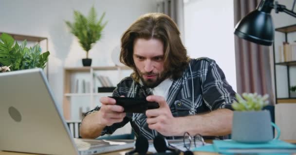 Portrait d'homme barbu heureux souriant heureux qui aime les jeux sur mobile à la maison et célébrer la victoire avec les mains en l'air, concept de loisirs — Video