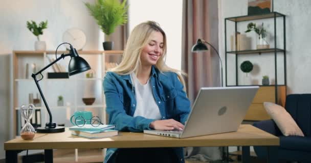 Belle jeune femme blonde moderne souriante assise au bureau à la maison et bavardant avec des amis sur ordinateur, concept de loisirs — Video