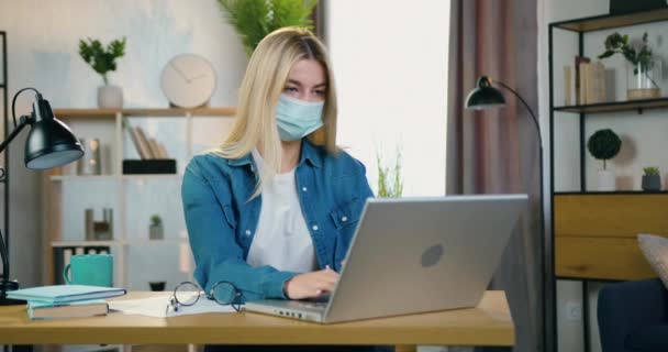 Çekici, konsantre, sarışın, yüz maskesi takan başarılı kadın çalışan, Coronavirus Pandemia 'nın kendini izolasyonu sırasında ev bilgisayarında çalışıyor. — Stok video