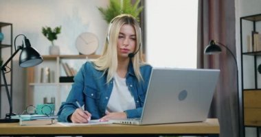 Evde eğitim kavramı, üniversite öğretmeniyle çevrimiçi video toplantısı sırasında kulaklık takan ve notlar alan çekici, kendine güvenen akıllı bayan öğrencinin...