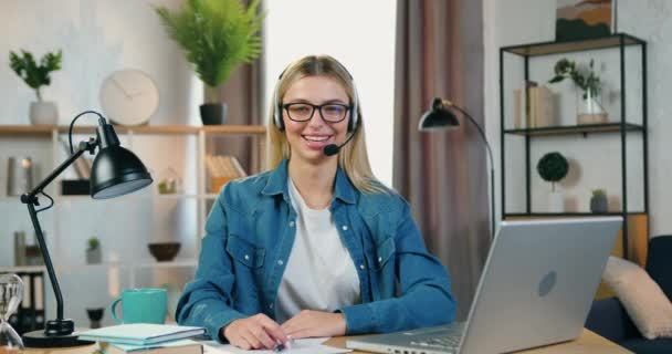 Žena portrét dobře vypadající usmívající šťastný úspěšný blond freelancer ve sluchátkách, které sedí na svém pracovišti v domácí kanceláři a gestikuluje palce nahoru do kamery — Stock video