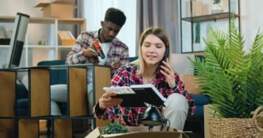 Güzel, mutlu, gülümseyen sarışın kız telefon görüşmeleri sırasında kutuları açıyor. Bu sırada da yetenekli siyah tenli erkek arkadaşı tornavidayla rafları birleştiriyor.