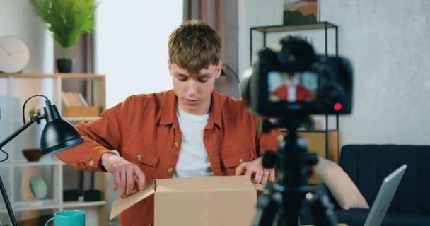 Гарний щасливий усміхнений здивований хлопець у модному одязі записує процес розпакування на камеру вдома і розмовляє зі своїми інтернет-послідовниками — стокове відео