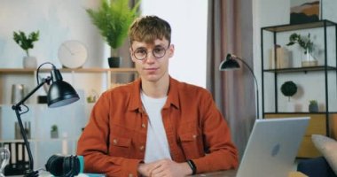 Yakışıklı, güler yüzlü, gözlüklü, modaya uygun kıyafetler giyen, kameranın önünde poz veren ve baş parmağını kaldıran genç, mutlu, sarışın adam.