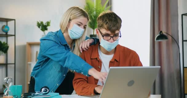 Ελκυστική αυτοπεποίθηση επιδέξιοι επαγγελματίες νέοι ελεύθεροι επαγγελματίες σε προσώπου ιατρικές μάσκες εργάζονται μαζί στο σπίτι και αναλύοντας λεπτομέρειες του έργου εκκίνησης, προστασία του covid-19 — Αρχείο Βίντεο