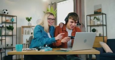 Kulaklıklı yakışıklı, duygusal ve kaygısız bir genç kız arkadaşı desteklemek için dizüstü bilgisayar oyunlarından zevk alıyor ve kazandıklarında eğleniyorlar ve beşlik çakıyorlar.