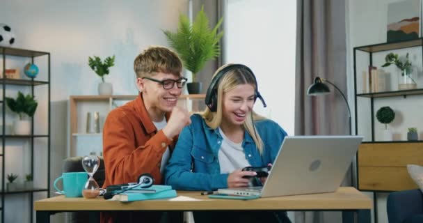 Πορτρέτο του ελκυστικού ευτυχισμένο χαμογελαστό νεαρό ζευγάρι που χαίρεται από τη νίκη σε βιντεοπαιχνίδια στο laptop και δίνοντας υψηλό πέντε ο ένας τον άλλο, αργή κίνηση — Αρχείο Βίντεο