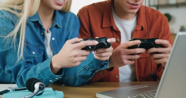 Attrayant sourire émotionnel jeune couple assis devant un ordinateur portable et jouer à des jeux vidéo avec joysticks tenant loisirs conjoints à la maison, gros plan — Video