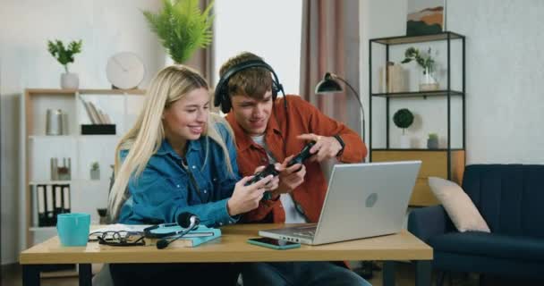 Buena apariencia alegre divertida pareja joven disfrutando de videojuegos en el ordenador portátil en casa y sintiendo la felicidad se convierten en ganar y levantar las manos, concepto de ocio — Vídeo de stock