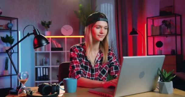 Trevlig glad glad ljushårig snygg ung kvinna som arbetar på datorn hemma på kvällen och tittar in i kameran med uppriktigt leende, framifrån — Stockvideo