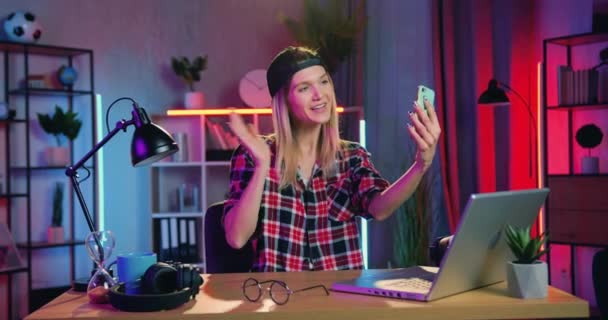 Bedårande leende glad ung modern blondin med örhänge i näsan med videocall på mobilen med vän eller relaitve när du sitter vid skrivbordet hemma på kvällen — Stockvideo
