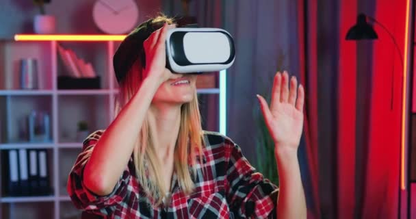 Close-up van mooie glimlachende zorgeloze jonge blonde meisje die het toepassen van virtual reality headset tijdens het werken thuis in de avond, moderne technologie concept — Stockvideo