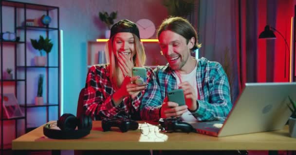 Lovely bahagia tersenyum dengan damai pasangan muda yang menikmati dari meninjau video lucu atau foto di smartphone mereka di rumah dengan pencahayaan malam, pandangan depan — Stok Video