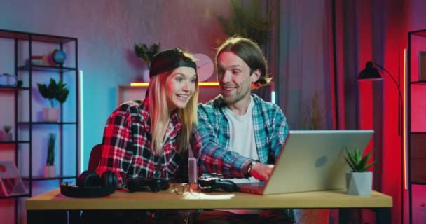 Attractive excited happy young loving couple see good news on laptop screen and rejoycing with high five and huggs,sitting at the table in contemporary room with night lighting — Stock Video