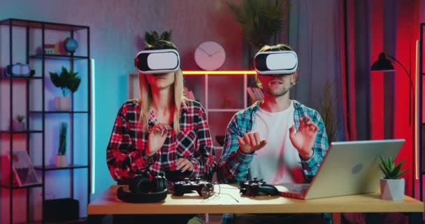 Достойная доверия умная современная пара, сидящая вечером за совместным рабочим местом дома и работающая в гарнитуре виртуальной реальности. — стоковое видео