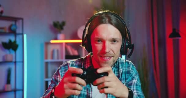 Närbild porträtt av attraktiva känslomässigt nöjda glada unga skäggiga spelare i hörlurar som njuter av sin seger i videospel hemma i moderna nattrum — Stockvideo