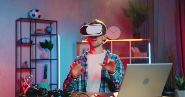 Привлекательный уверенный умный бородатый парень в наушниках виртуальной реальности, работающий на воображаемом дисплее в домашнем офисе вечером, современная технологическая концепция — стоковое видео