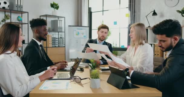 Aantrekkelijke moderne slimme succesvolle mixed race collega 's zitten aan kantoor tafel en het krijgen van bedrijfsstatistieken met grafieken van de belangrijkste mannelijke manager tijdens de vergadering in bedrijf — Stockvideo