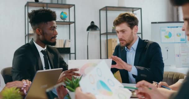 Handsome positive skilled bearded businessman talking with black-skinned partner and explaining financial report during joint meeting in office room — Stock Video