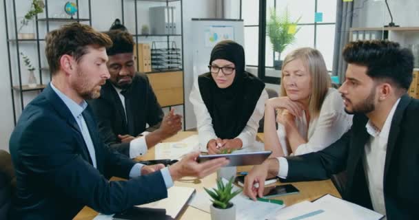 Nahaufnahme eines angenehmen selbstbewussten, hart arbeitenden multiethnischen Teams, das in einem modernen Büroraum mit Tablet-Gerät zusammenarbeitet — Stockvideo