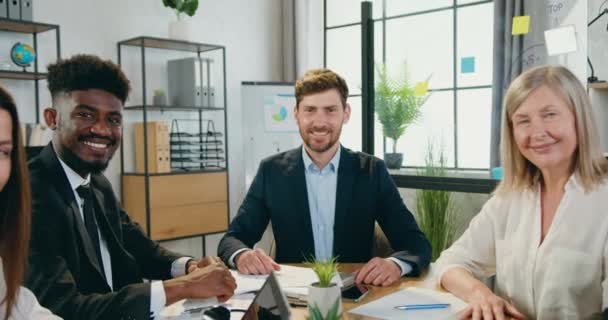 魅力的な笑顔幸せなプロの多様なチームの企業の同僚のカメラの前に近代的なオフィスの部屋に座って親指を表示し、閉じる — ストック動画