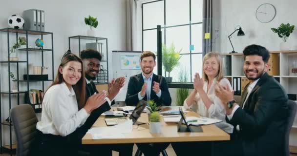 Geschäftliches Erfolgskonzept, bei dem attraktive lächelnde zufriedene internationale Geschäftsleute am Arbeitsplatz im Sitzungssaal sitzen und in die Hände klatschen und vor der Kamera posieren — Stockvideo