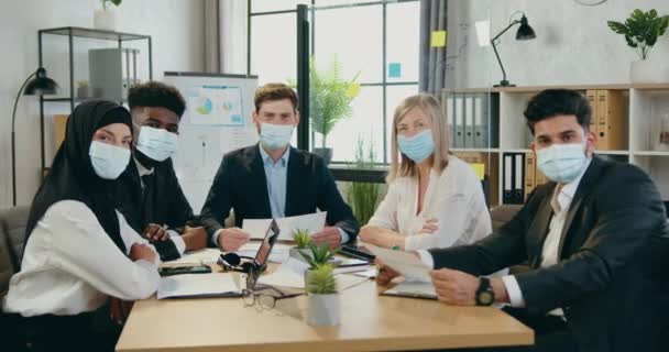 Preventie covid-19 infectie concept waar goed uitziende zelfverzekerde ervaren multiraciale zakenmensen in beschermende maskers op zoek naar camera in kantoor kamer — Stockvideo