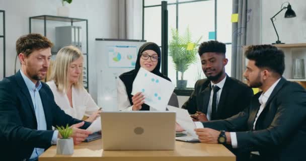Прекрасна усміхнена арабська бізнес-леді в Хіджабі проводить відеоконференцію разом з досвідченими різноманітними членами команди на ноутбуці і пояснює результати виконаної роботи для далеких партнерів — стокове відео